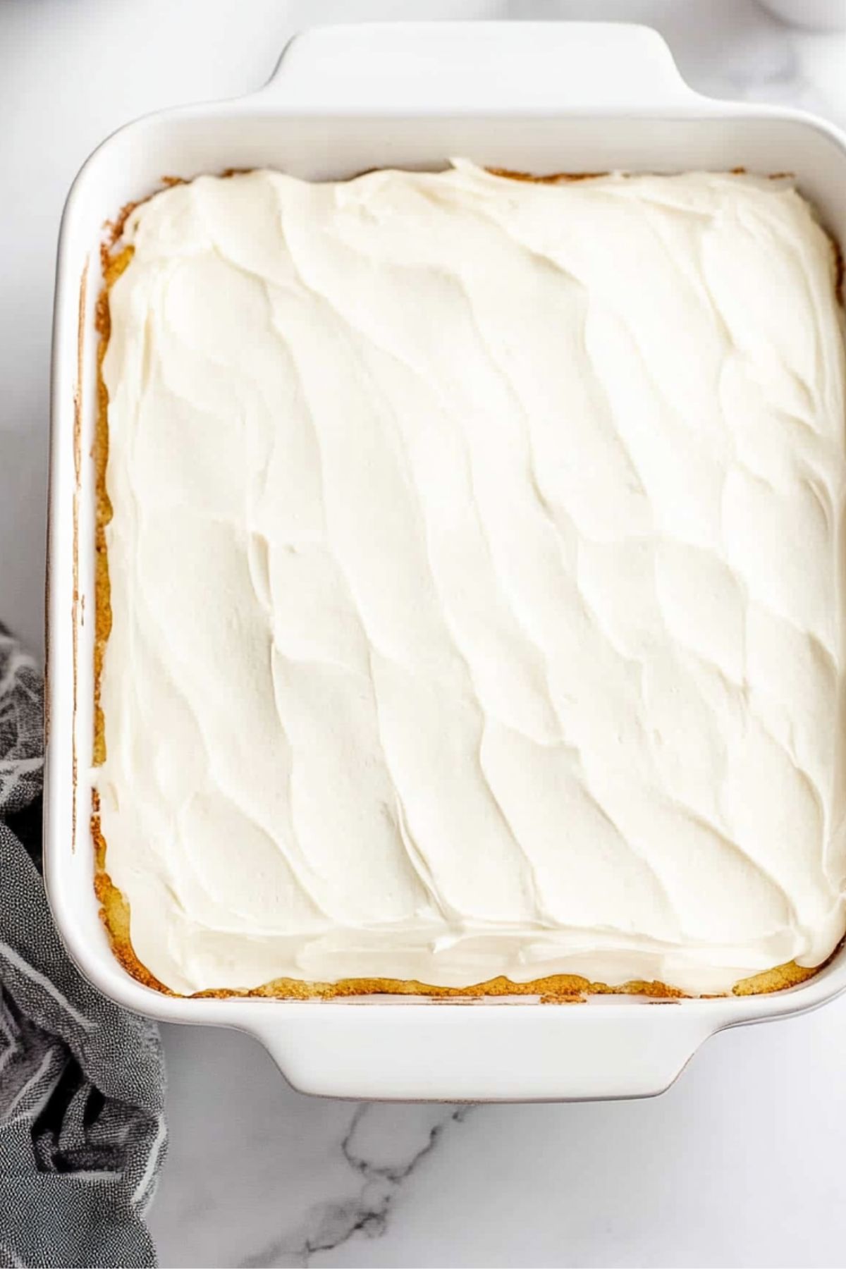 Cake covered with cream cheese frosting baked in a rectangular pan., top view