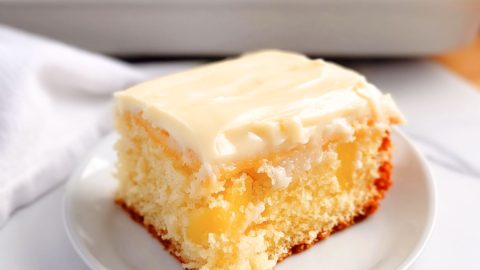 Square slice of moist cake with cream cheese frosting served on a white plate.