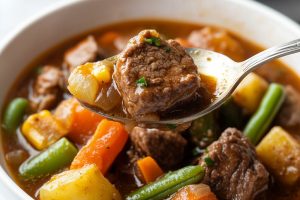 A close-up of mulligan stew in a large bowl, with tender beef and a colorful assortment of vegetables like carrots, green beans, and potatoes.