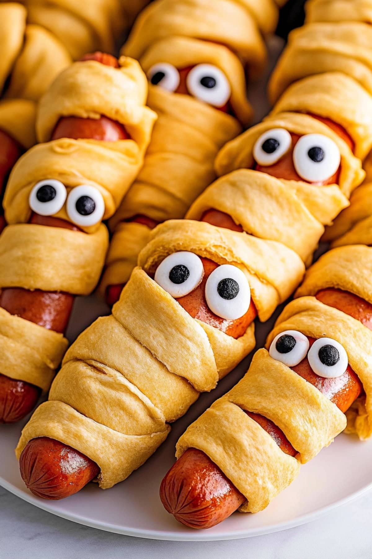 Close-up of a spooky mummy hot dog, wrapped in crescent dough with decorative eye candies.