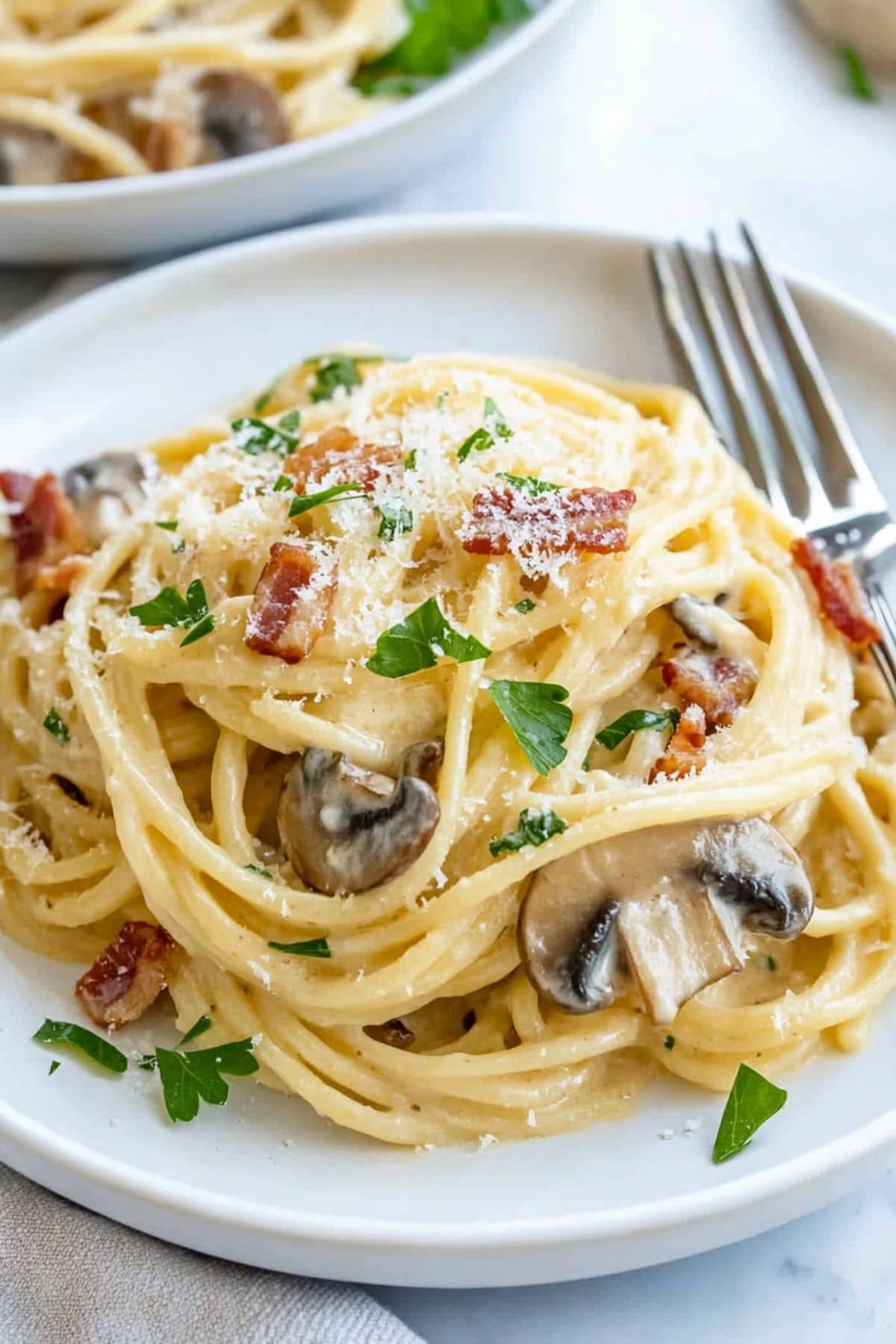 Serving of mushroom carbonara in a white plate, fork on the side.