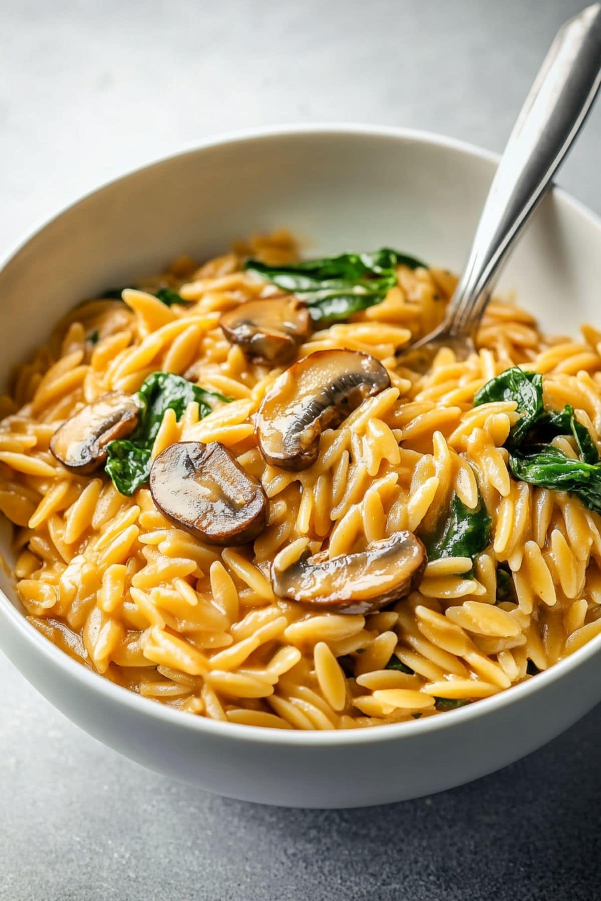 Mushroom orzo pasta served in a white bowl with spoon.