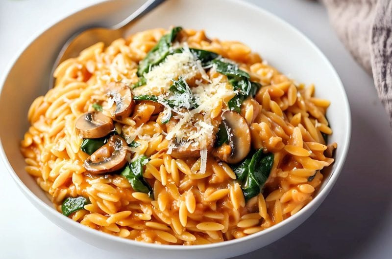 Mushroom orzo pasta with baby spinach served in a white bowl.