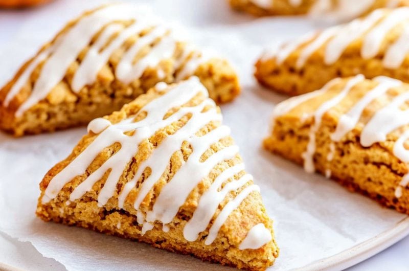 Pumpkin scones lying on top of parchment paper drizzled with white sugar.