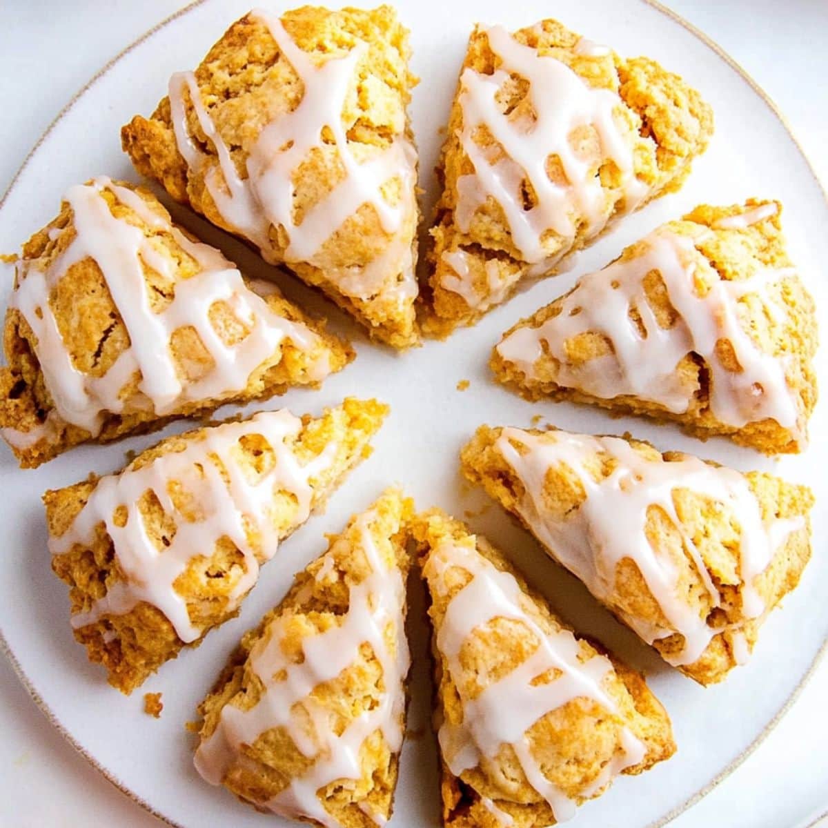 Arranged in circle pumpkin scones drizzled with white glaze served in a white plate.