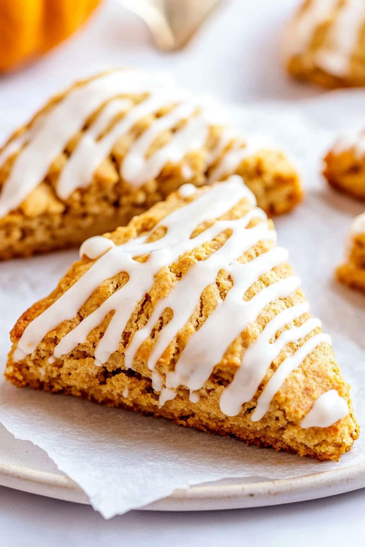 Pumpkin scones drizzled with white glaze sitting on top of white parchment paper.