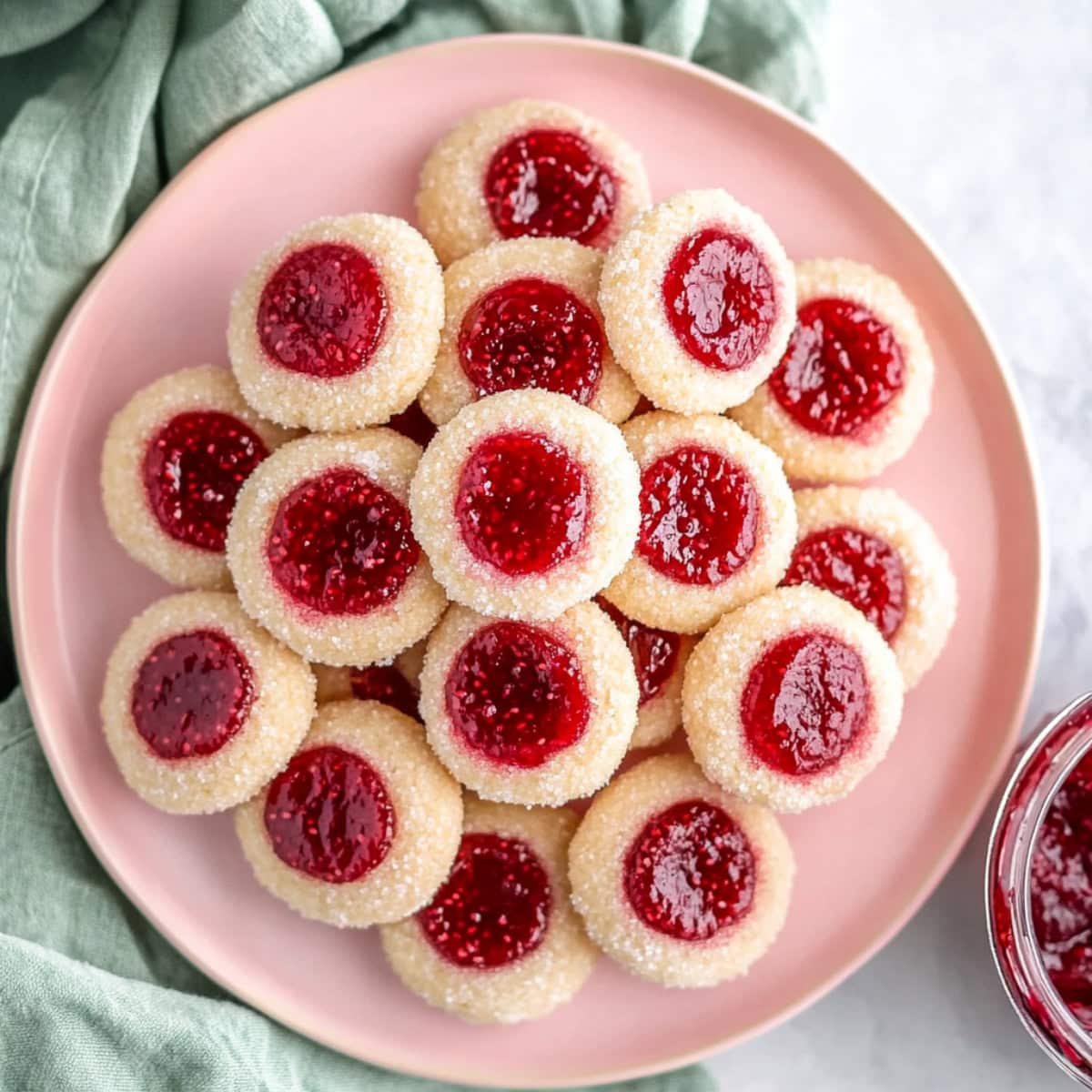 Overhead view of raspberry thumbprint cookies arranged on a pink plate.