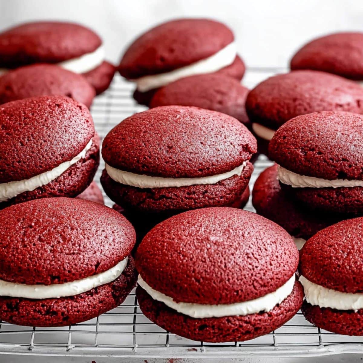 Red velvet whoopie pies with cream cheese filling arranged in a cooling rack.