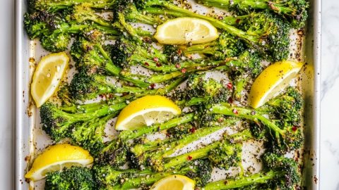 A baking sheet of roasted broccolini with lemon slices.