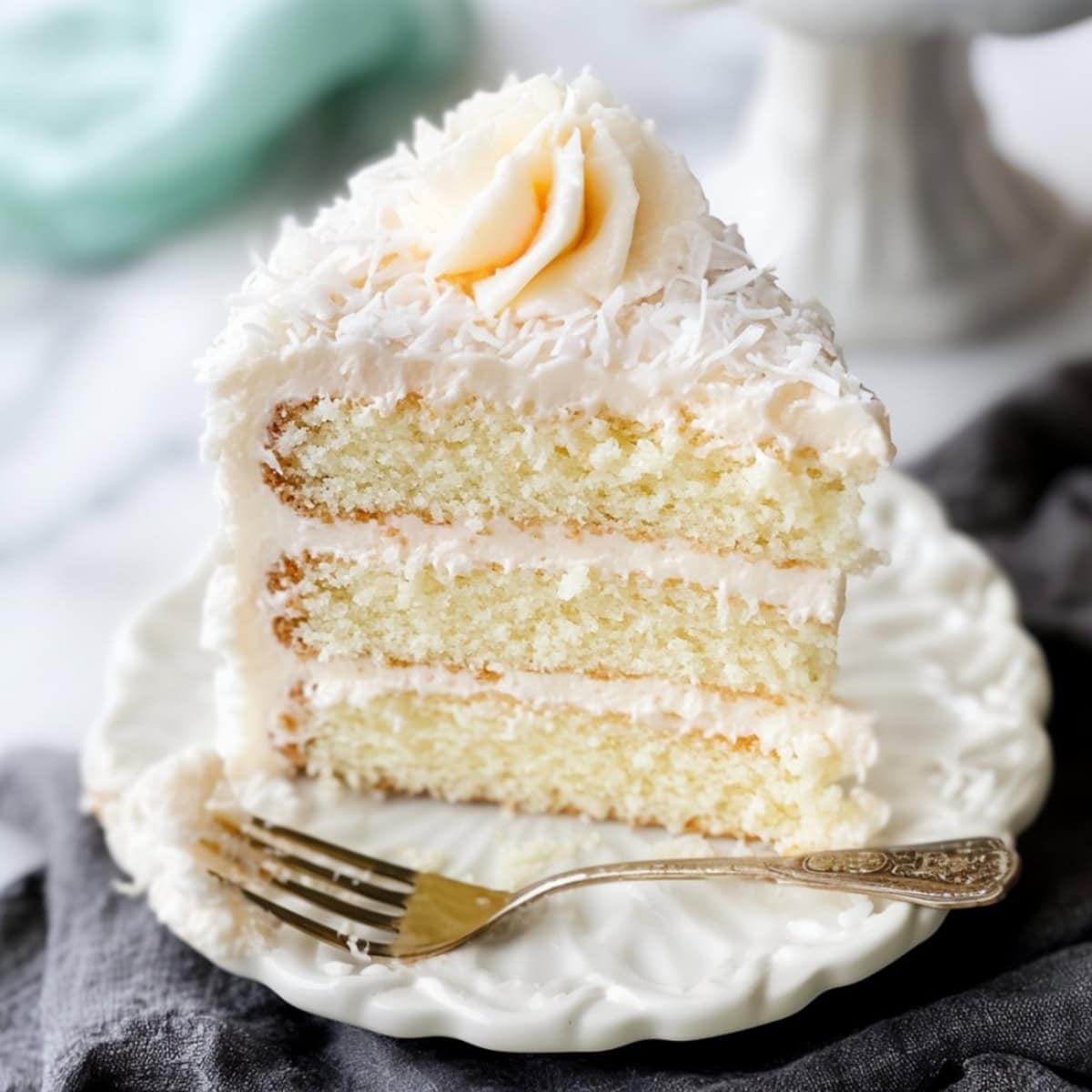 A moist coconut cake topped with a layer of shredded coconut, served on a white plate.