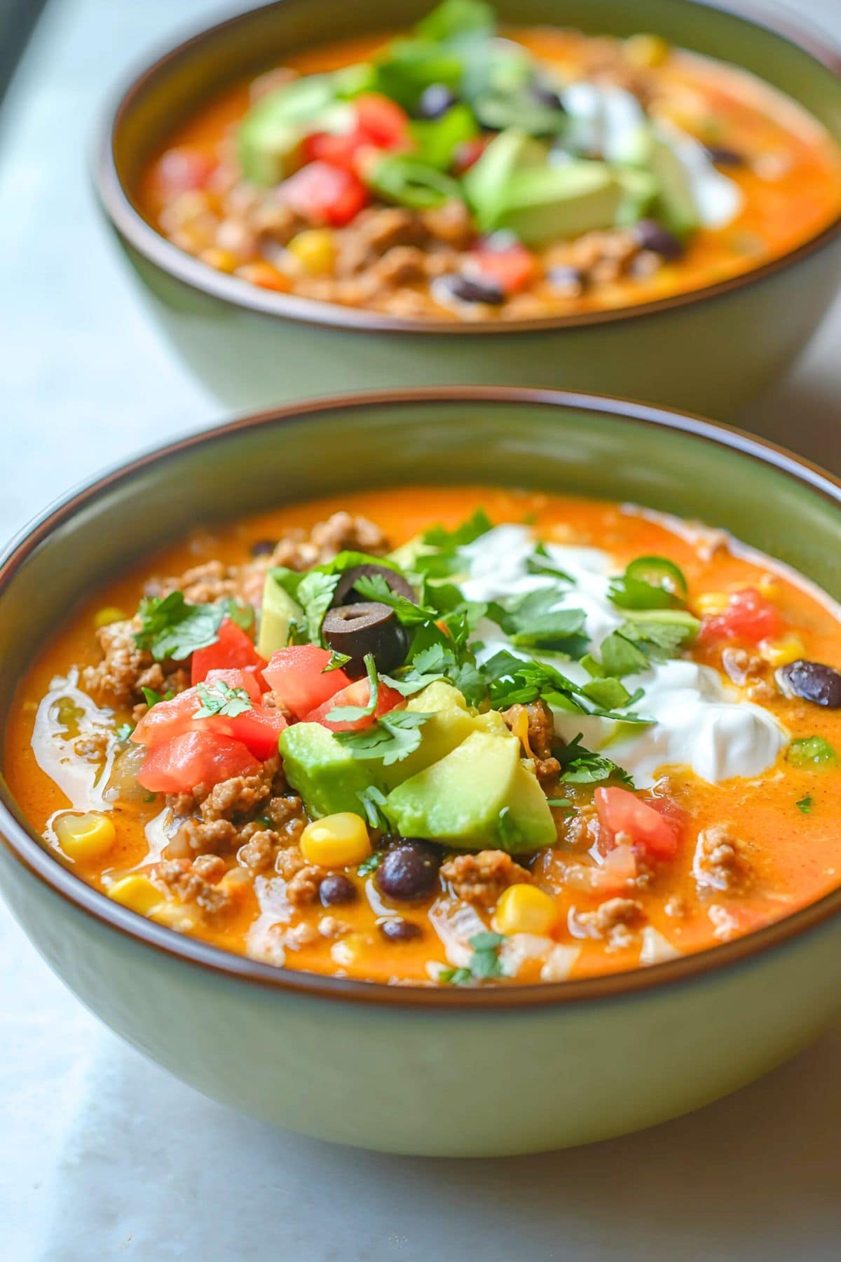 Slow cooker nacho soup served in green bowls garnished with salsa, avocado and sour cream.