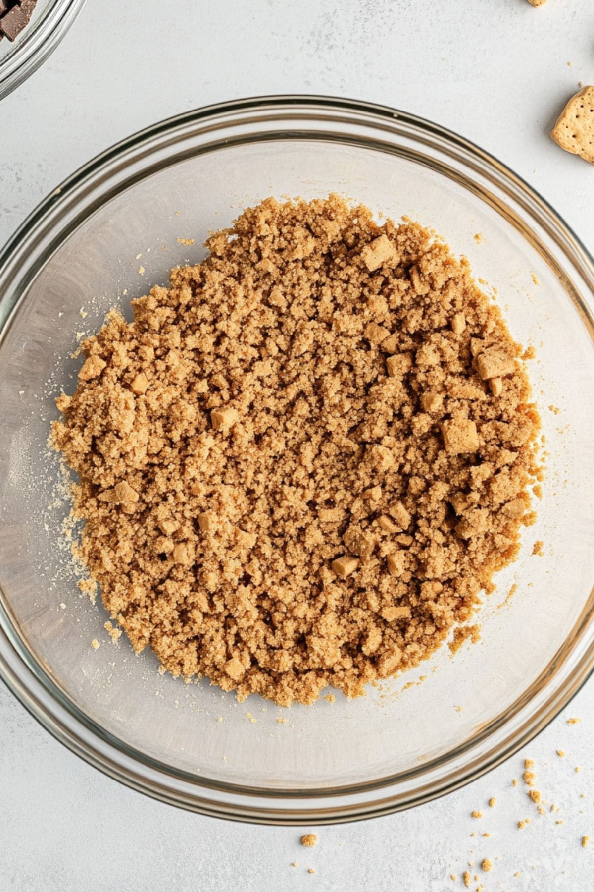 Crushed graham crackers mixed with melted butter in a glass bowl, top view 