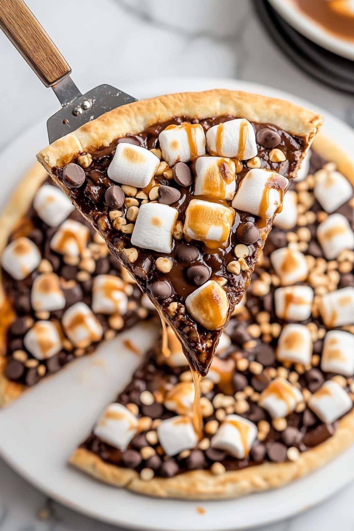 Sliced S'mores pizza lifted by a pie ladle sitting in a pie tray, close up, top view