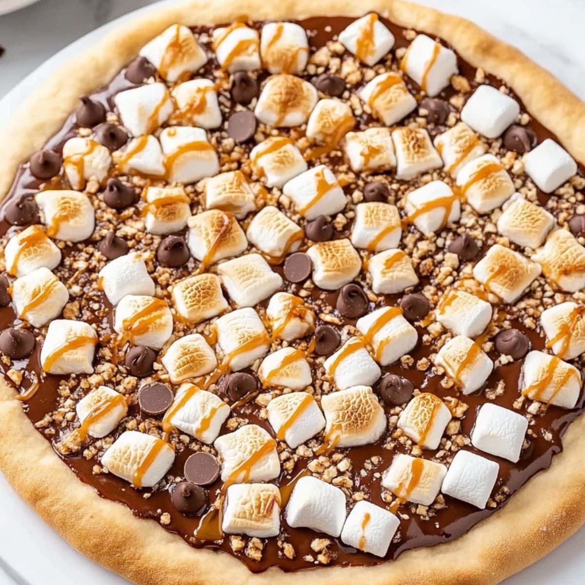 Whole S'more pizza with nutella, mini chocolate chips and mini marshmallows drizzled with caramel sauce.