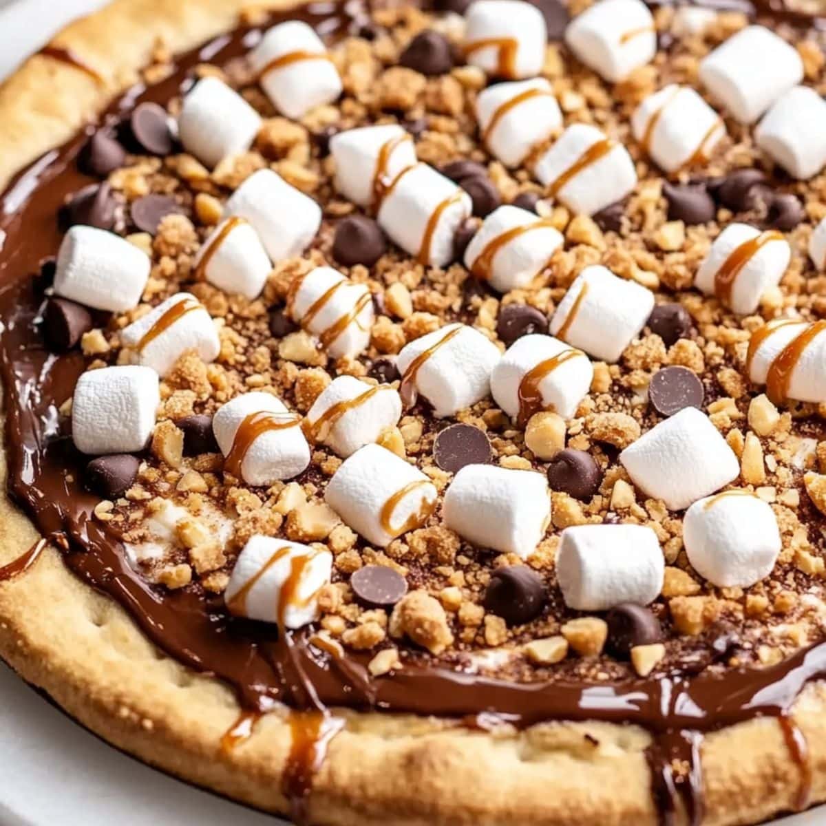 Whole Smore's dessert pizza with marshmallows and melted chocolate on top of baked pizza dough drizzled with caramel sauce