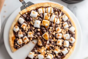 Sliced Smore's dessert pizza in a pie plate, slice lifted with a pie ladle.