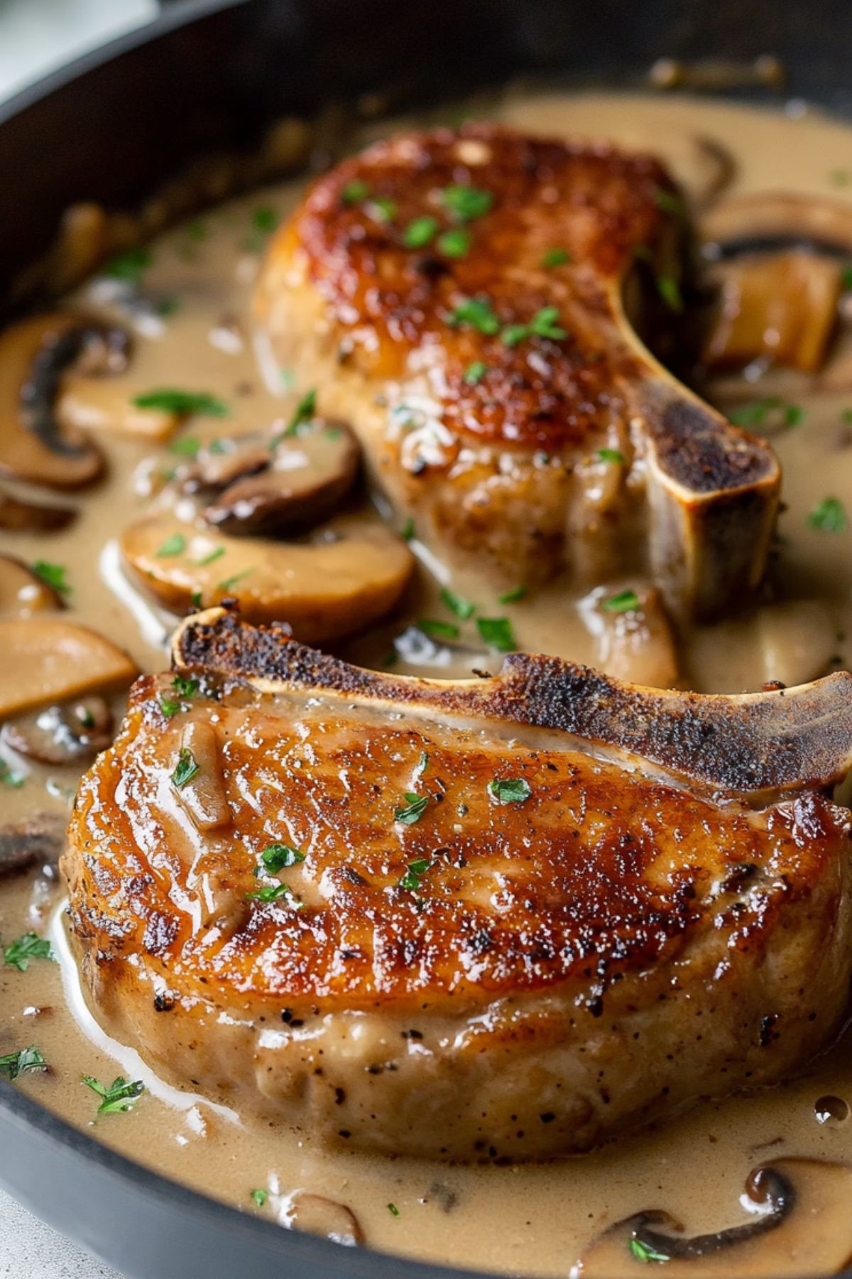 Pork chops smothered in mushroom gravy in skillet pan.