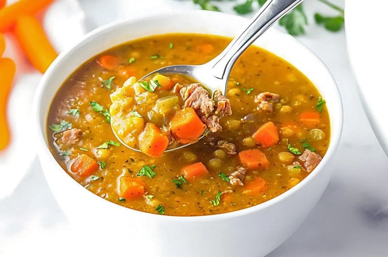 Spilt pea soup in a white bowl scooped with a spoon.