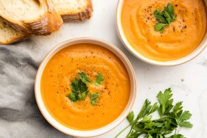 Two bowls of sweet potato and carrot soup, served with a side of bread.