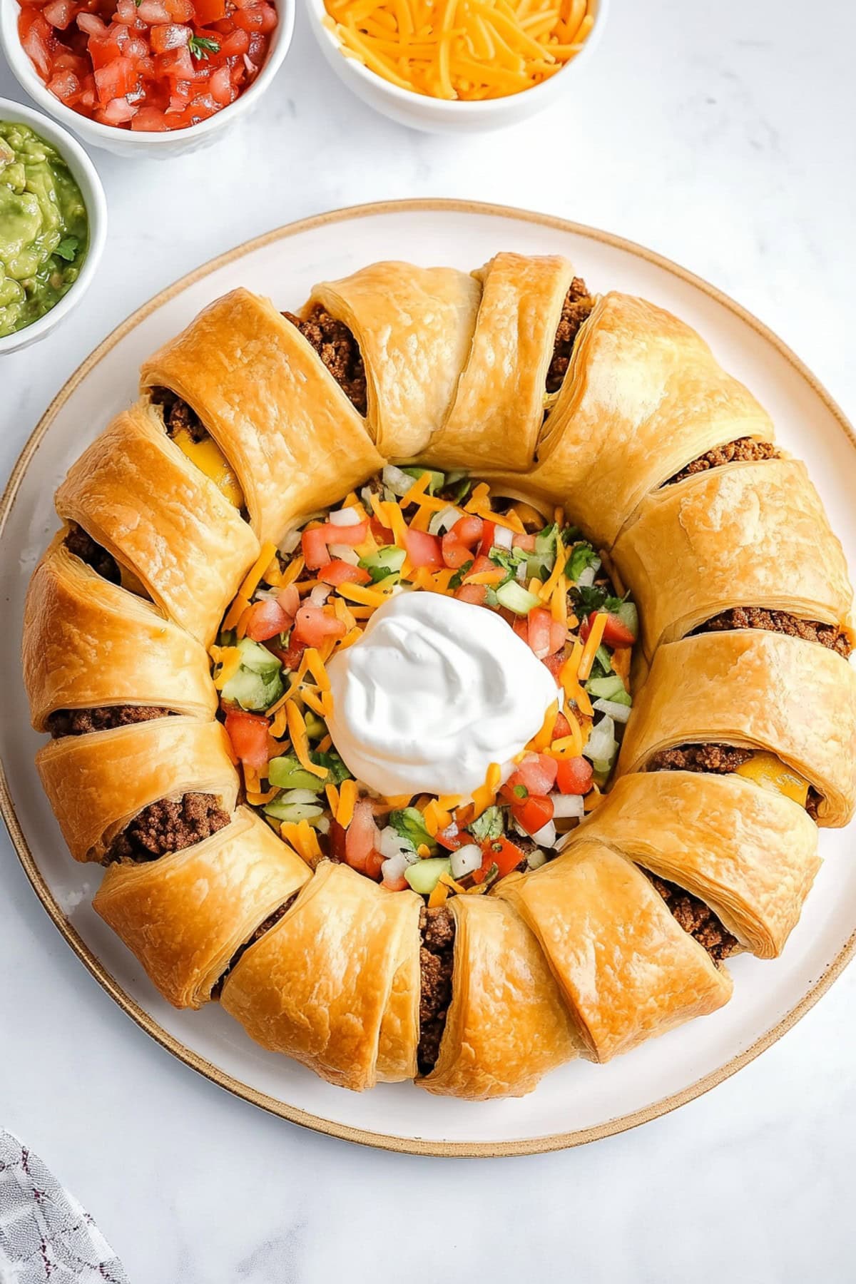 A perfectly baked taco ring with golden pastry, stuffed with taco-seasoned beef, served with salsa, shredded cheese, sour cream and shredded lettuce for toppings.