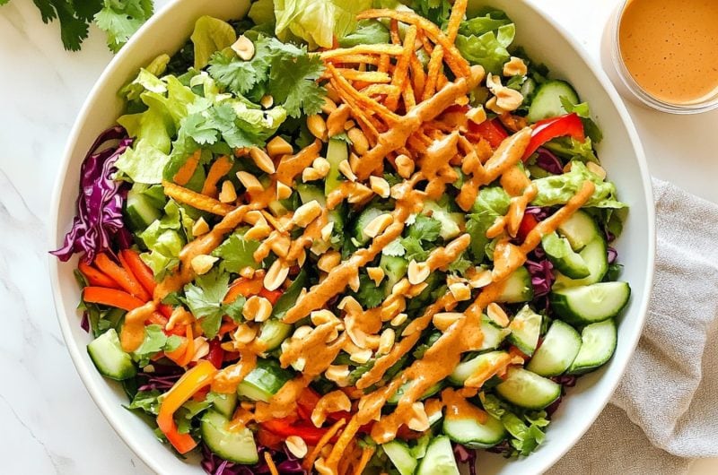 Bright Thai crunch salad with shredded veggies and a side of peanut butter dressing in a small bowl.