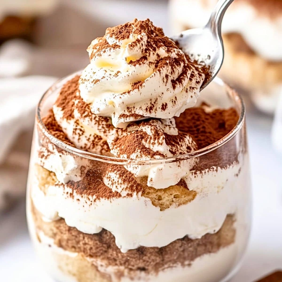 Spoon scooping mascarpone cream from tiramisu in a cup.