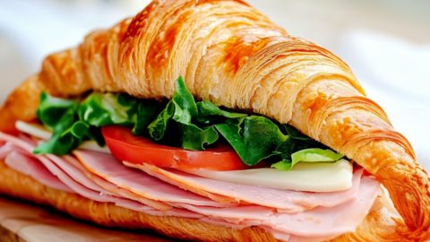 Turkey croissant sandwich sitting on a wooden board.