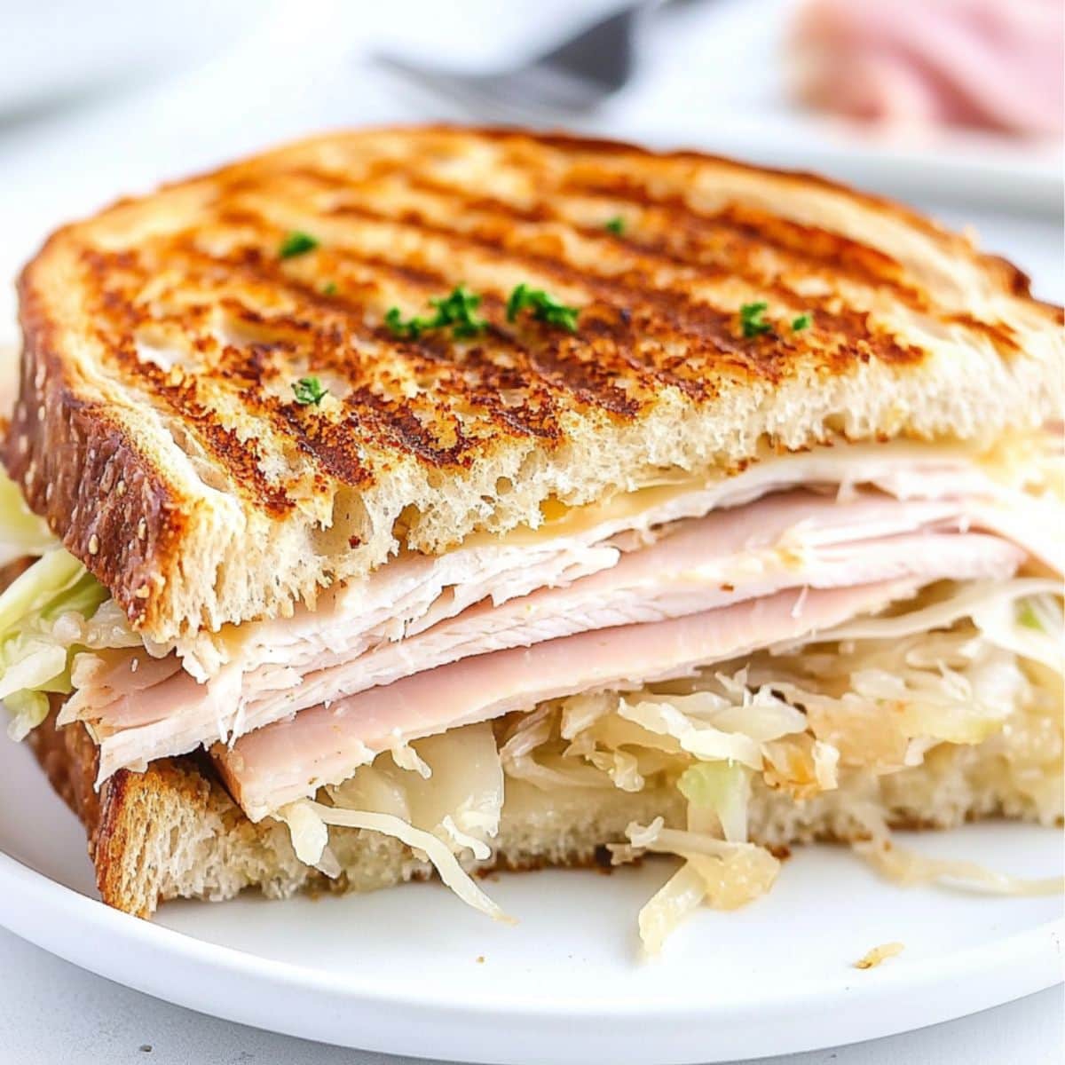 Sandwich sliced in half with sauerkraut, turkey and melted cheese filling served on a white plate.