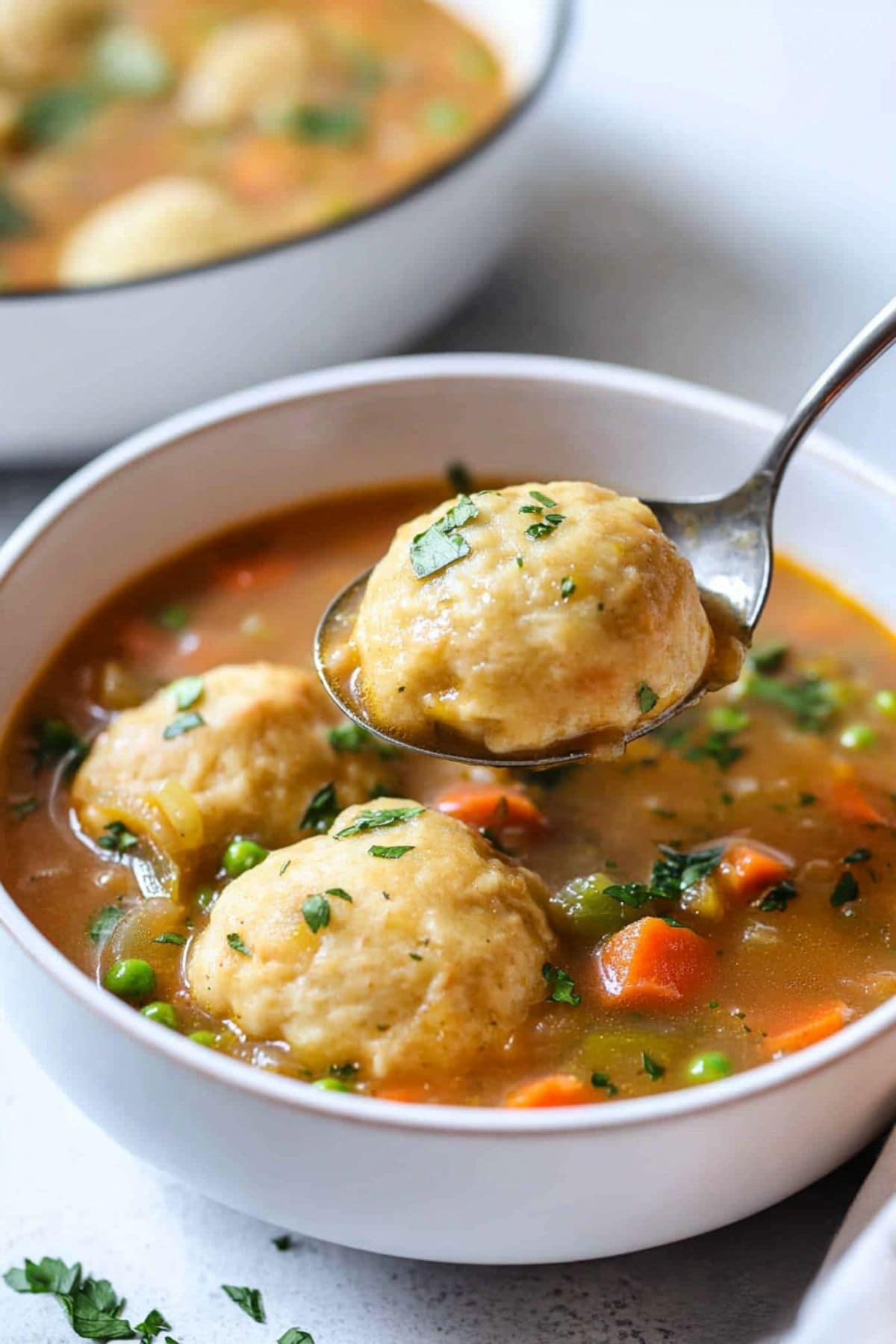 Spoon scooping a dumpling from a serving of vegetable stew in a white bowl