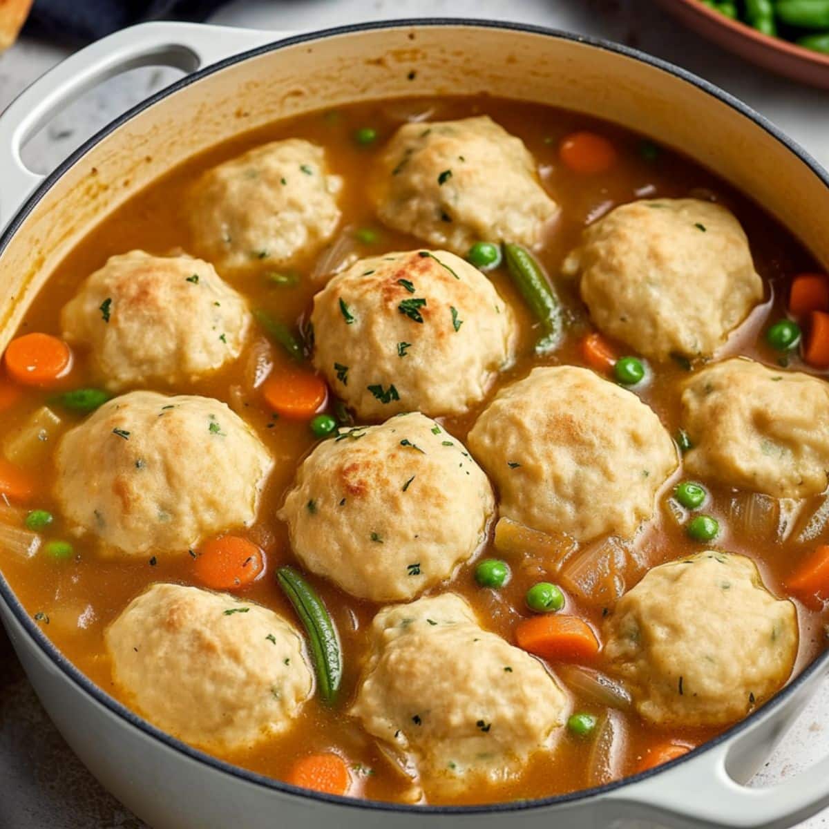 Vegetable stew with green peas, carrots and tomato based soup cooked in a white pot.