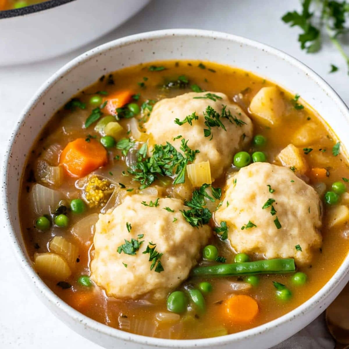 Vegetable stew with green peas, carrots and tomatoes with floating dumplings served in a white bowl.