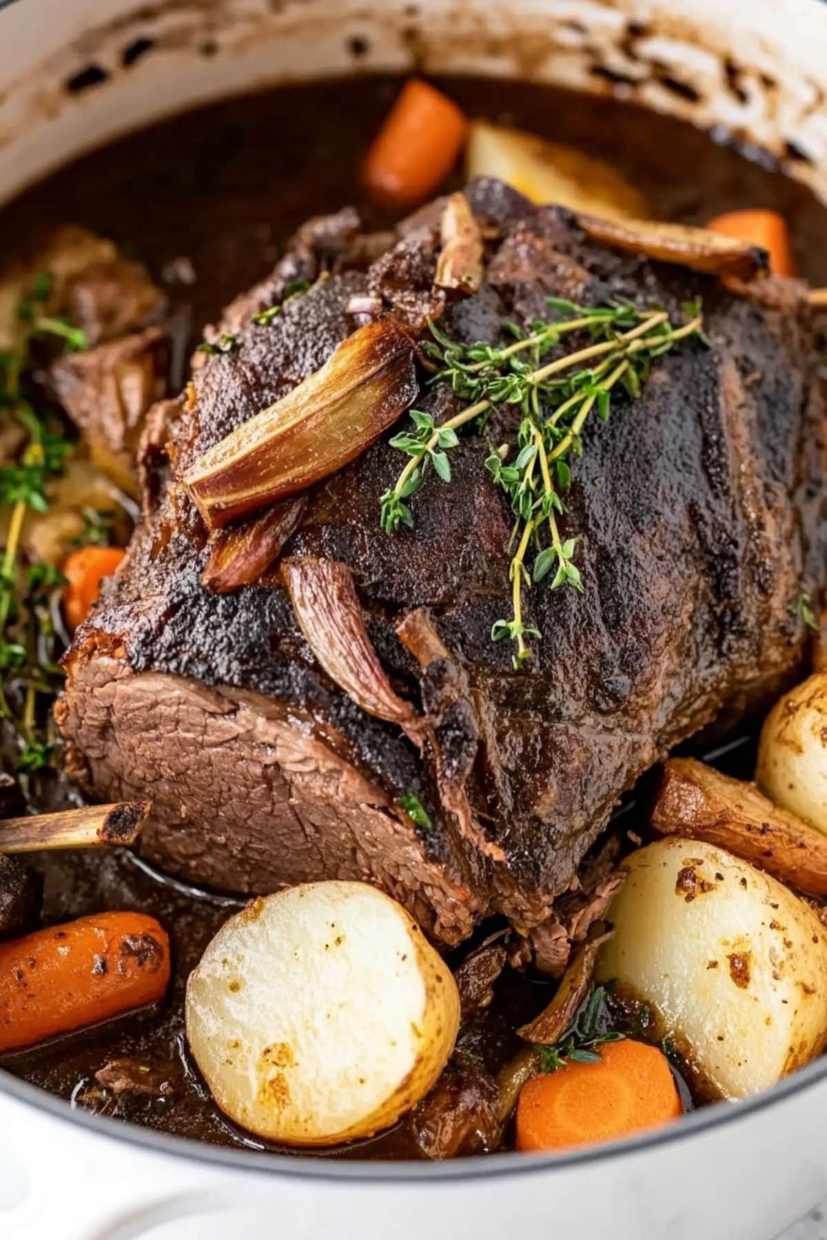 Chuck roast cooked with potatoes, carrots herbs and onions with savory sauce inside a Dutch oven. 