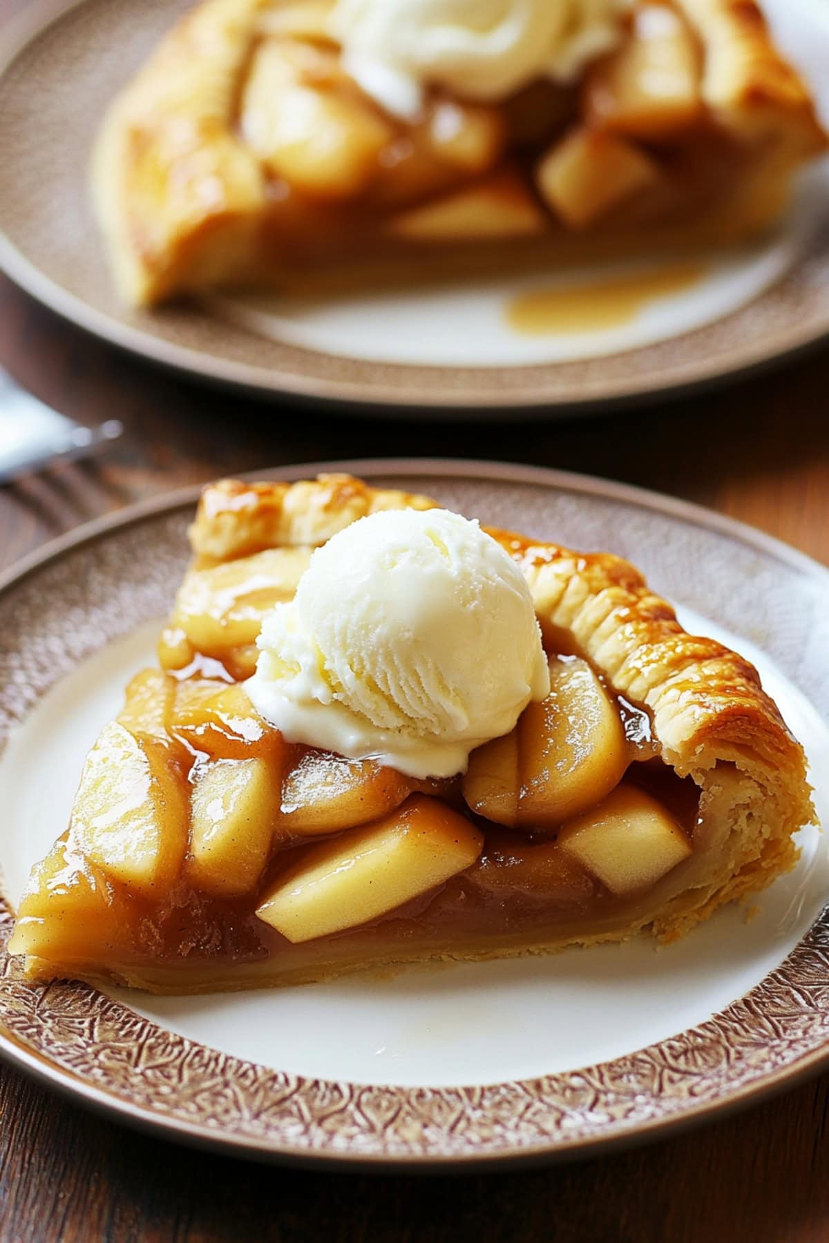 Two slices of apple galette on plates topped with ice cream.