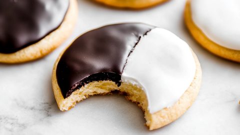 Black and White cookies on a marble table, one has a bite removed