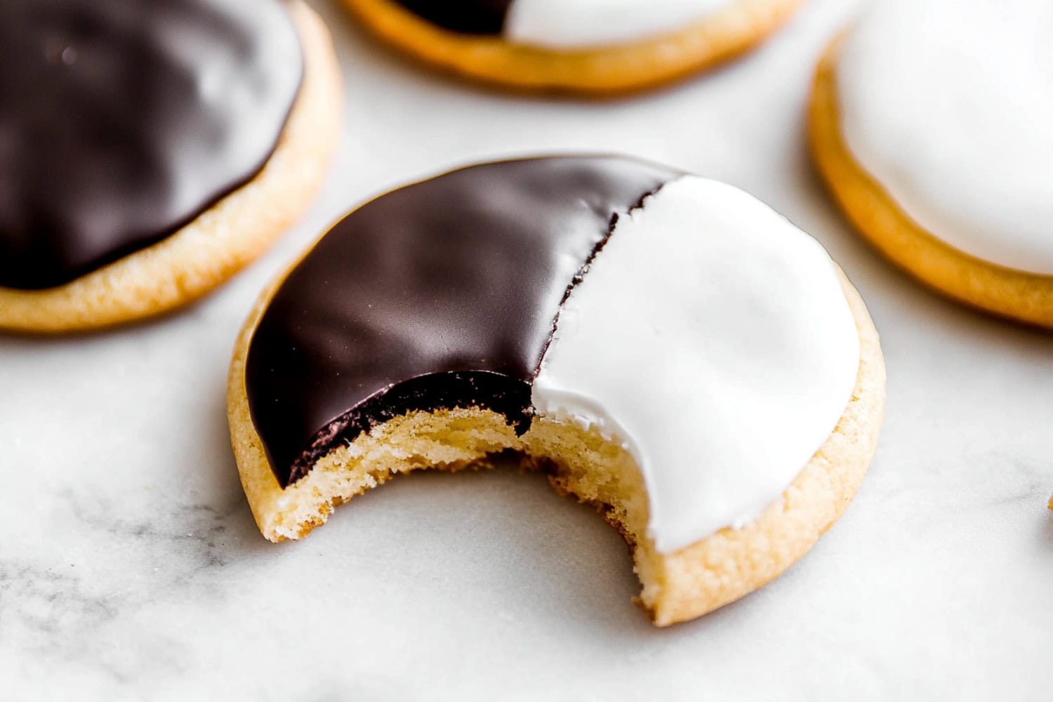 Black and White cookies on a marble table, one has a bite removed