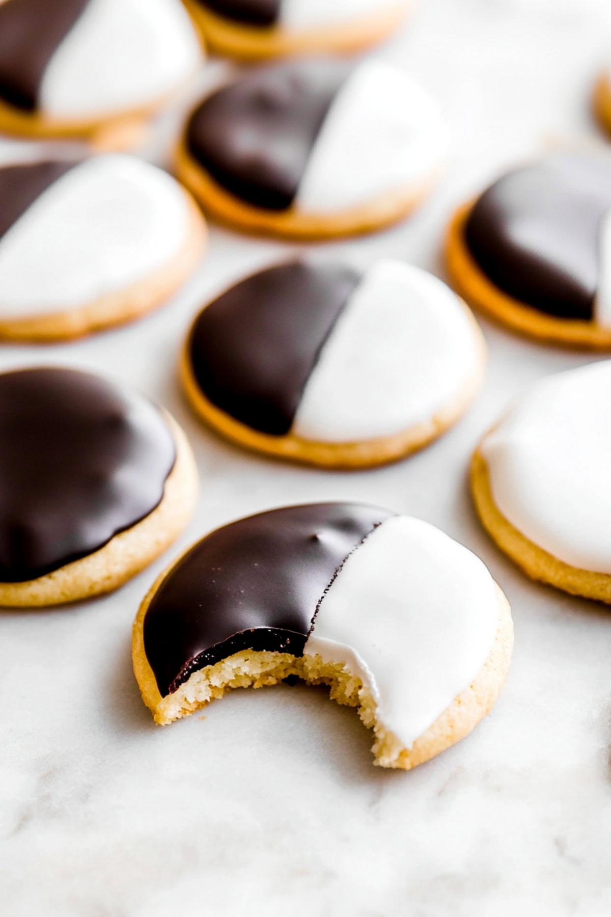 Bakery-style black and white cookies on a marble table, one has a bite removed