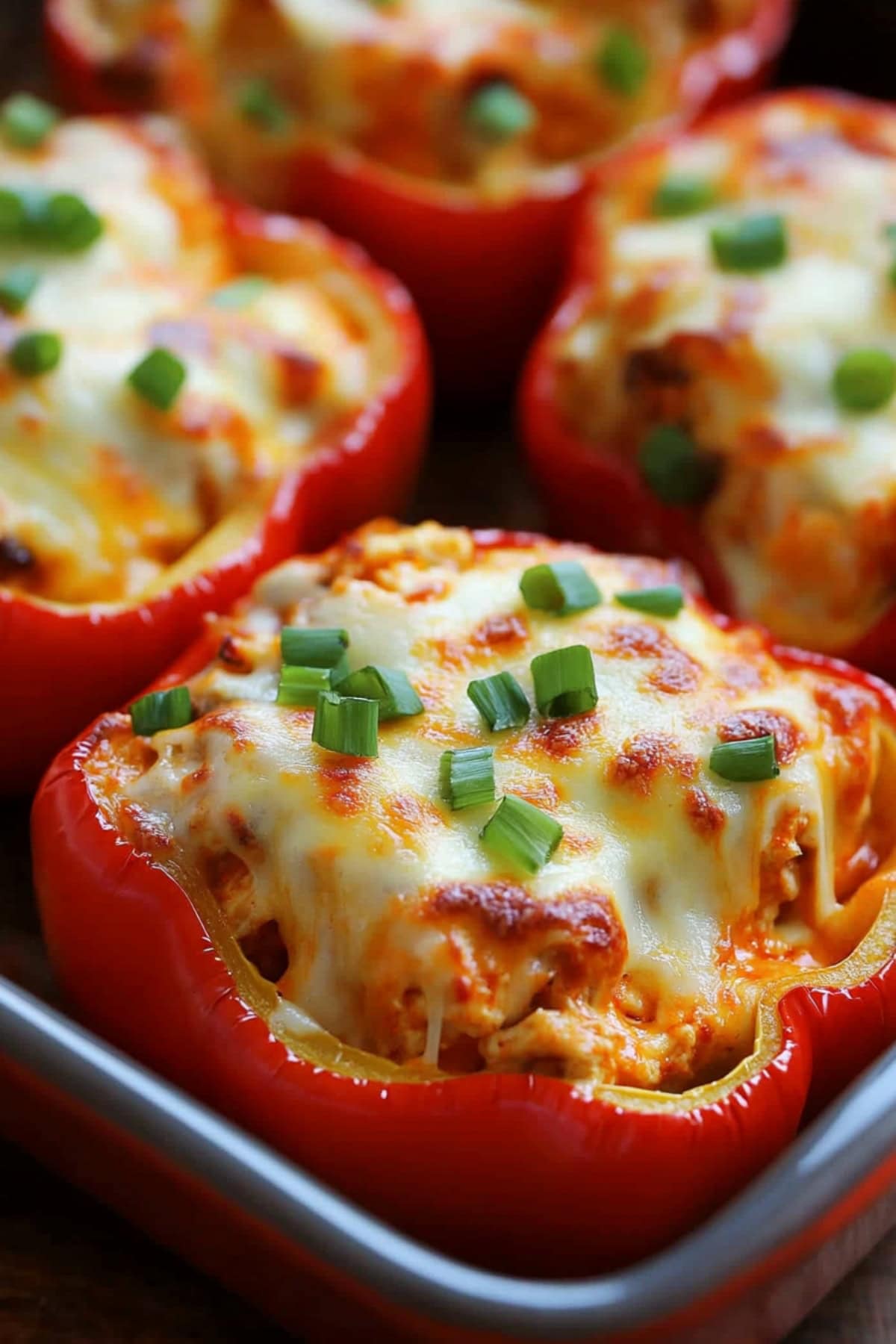 Peppers stuffed with buffalo flavored shredded chicken, covered with melted cheese sitting on a baking pan.