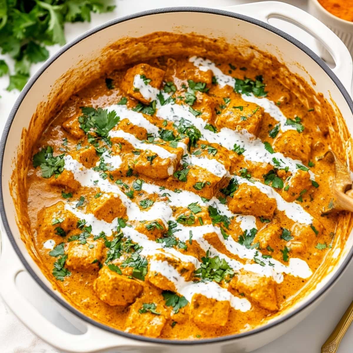 Chicken korma in a white pot drizzled with cream.