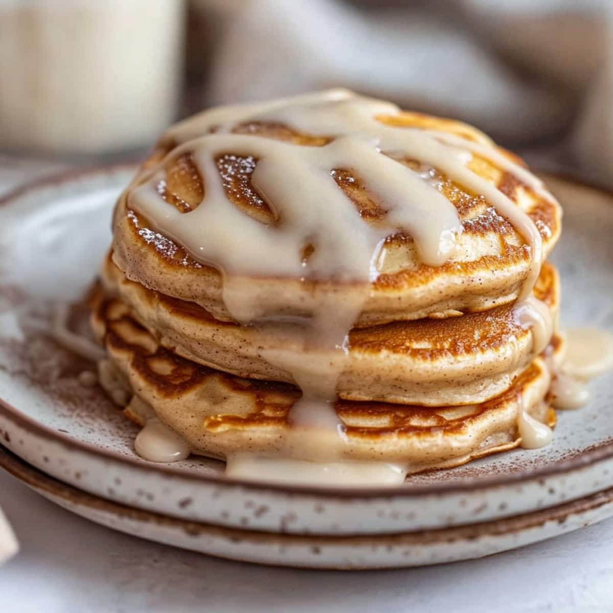 Cinnamon swirl pancakes stacked on a plate drizzled with cream cheese glaze.