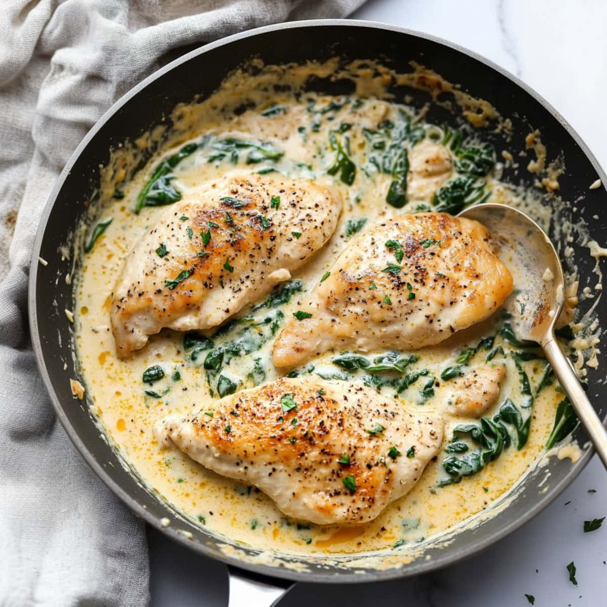 Chicken cooked in creamy sauce and spinach in a skillet pan.