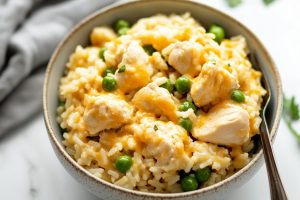 A bowl of creamy chicken and rice with cheese and green peas in a bowl.