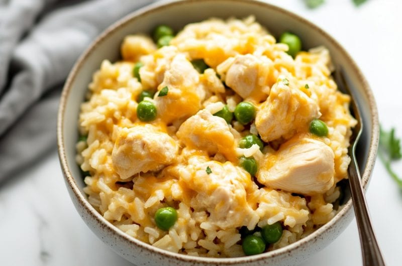 A bowl of creamy chicken and rice with cheese and green peas in a bowl.