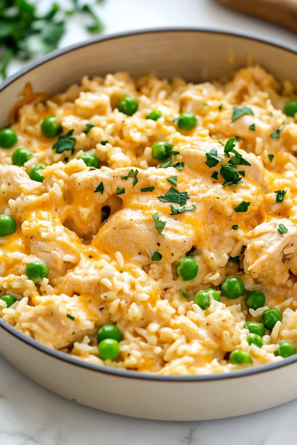 A close-up shot of creamy chicken and rice with peas and garnished with parsley in a large skillet.