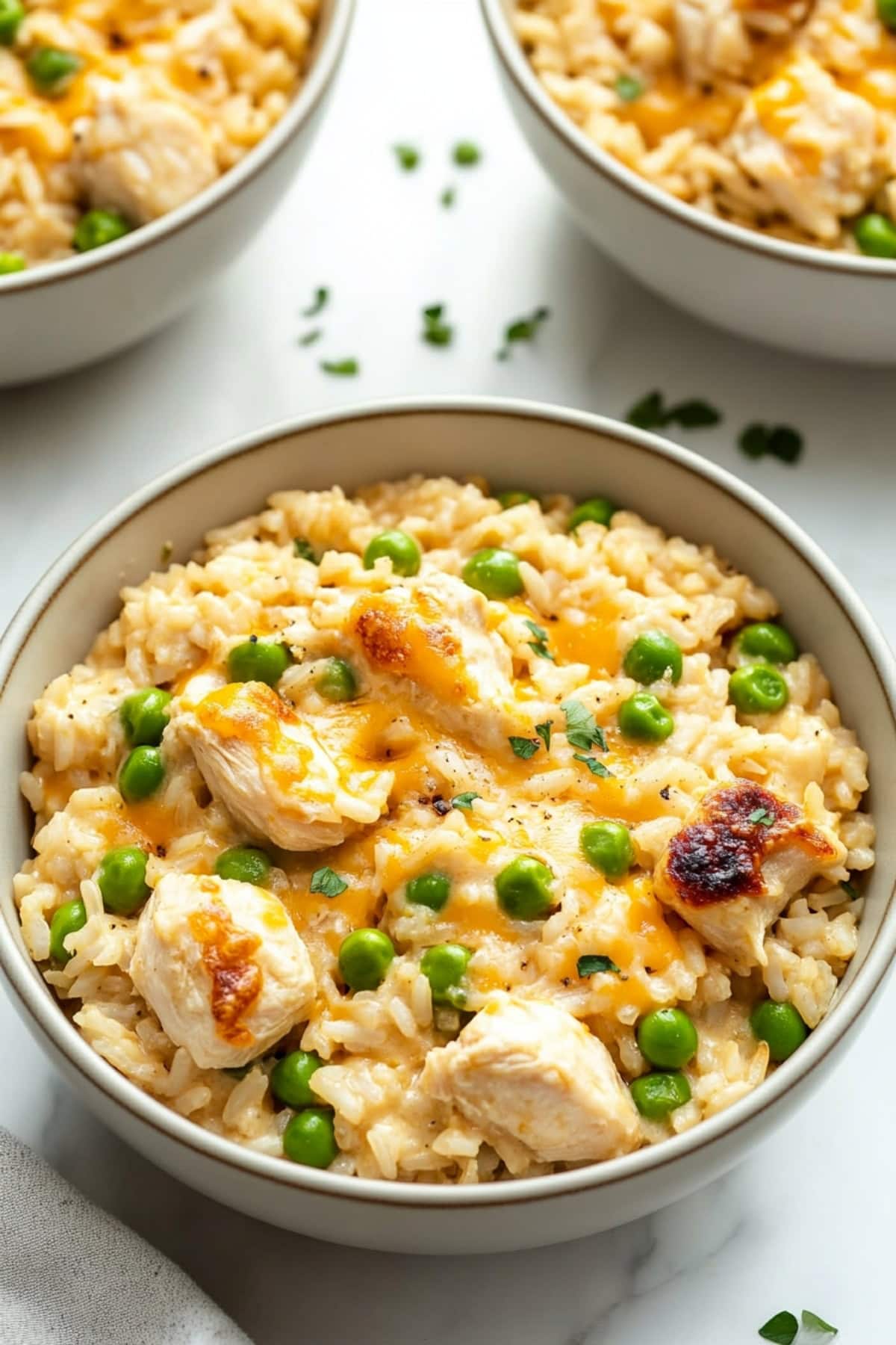 Three bowls of creamy chicken and rice with green peas.