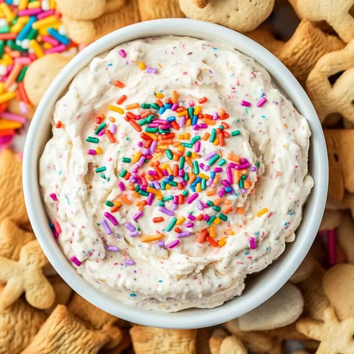 Colorful creamy dip with funfetti sprinkles served in a white bowl with animal crackers, top view