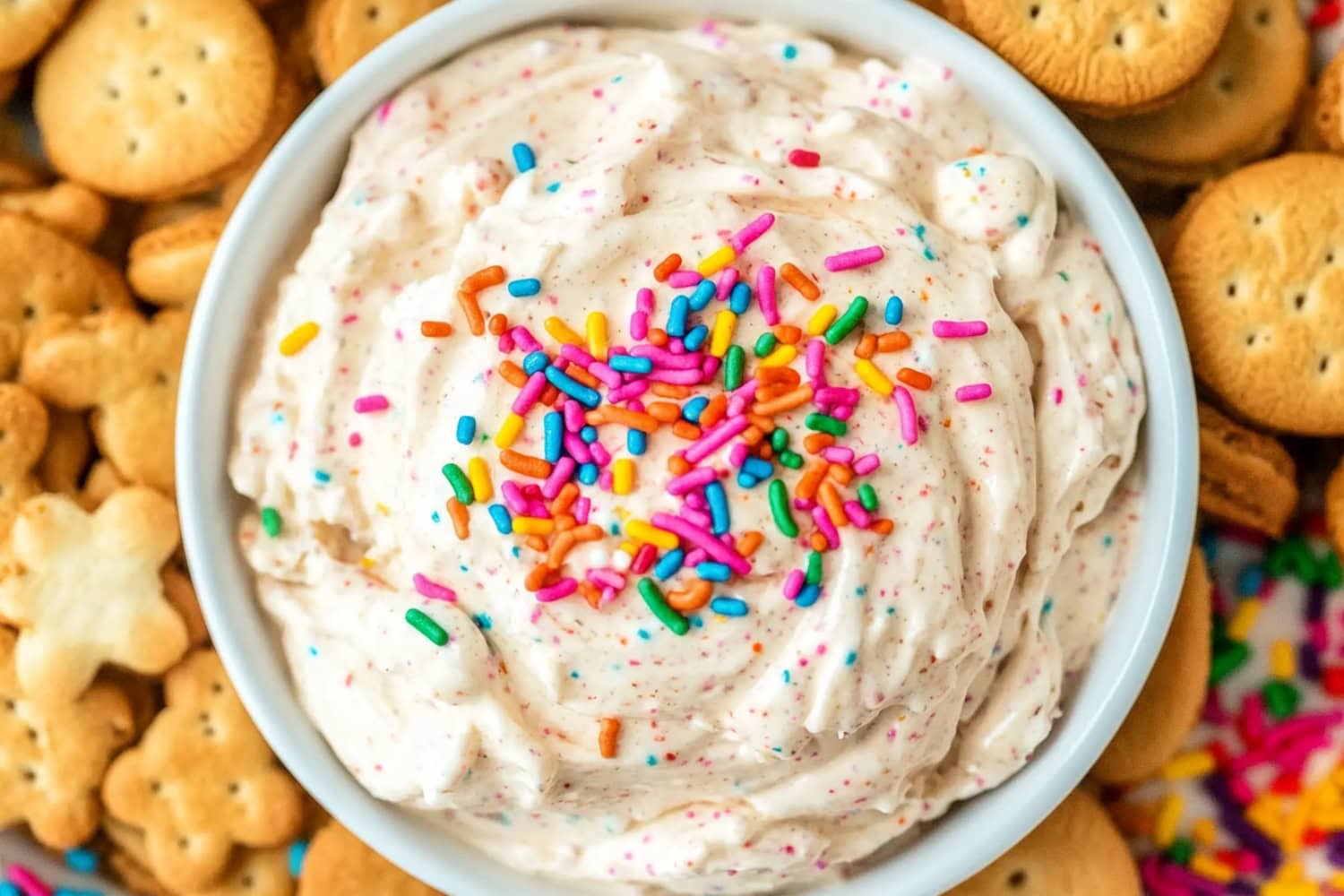 White creamy Dunkaroo dip in a white bowl garnished with Funfetti candies served with biscuits.