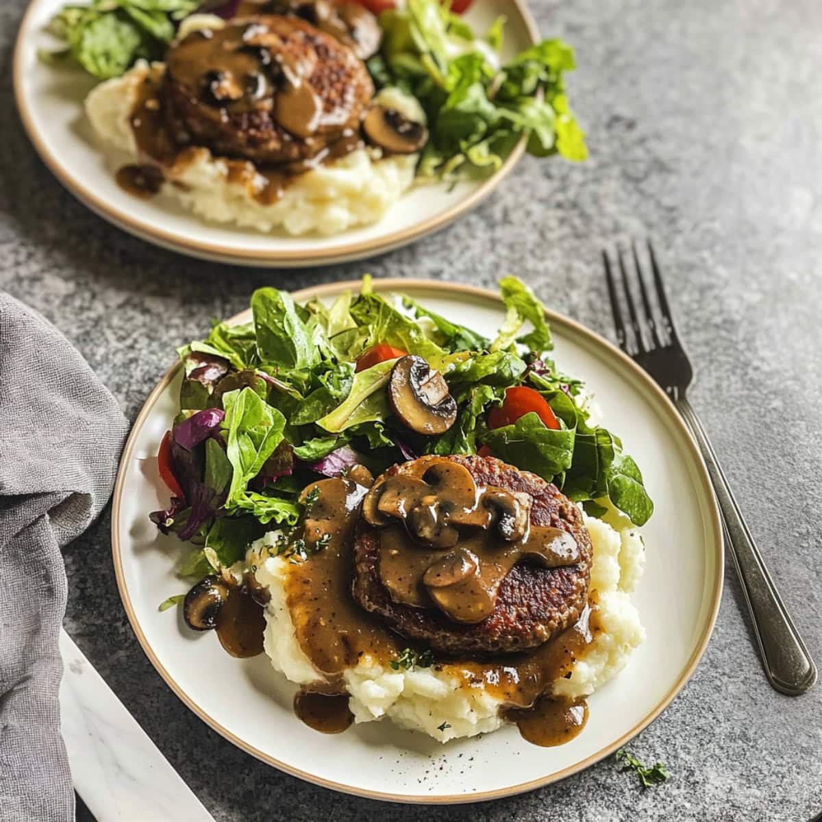 Two plates of hamburger steak with mashed potatoes and vegetables.