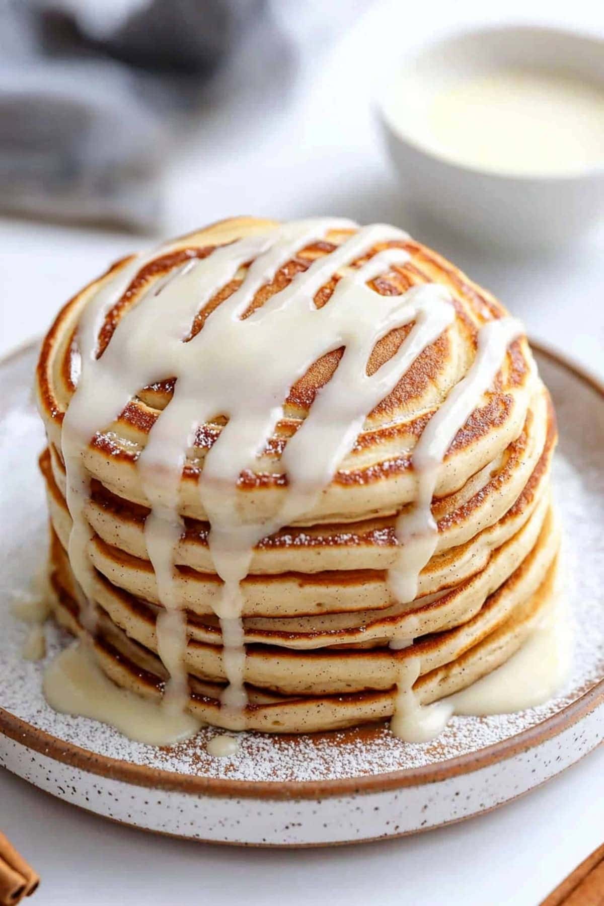 Cinnamon roll pancake stacked on a plate and drizzled with cream cheese glaze.