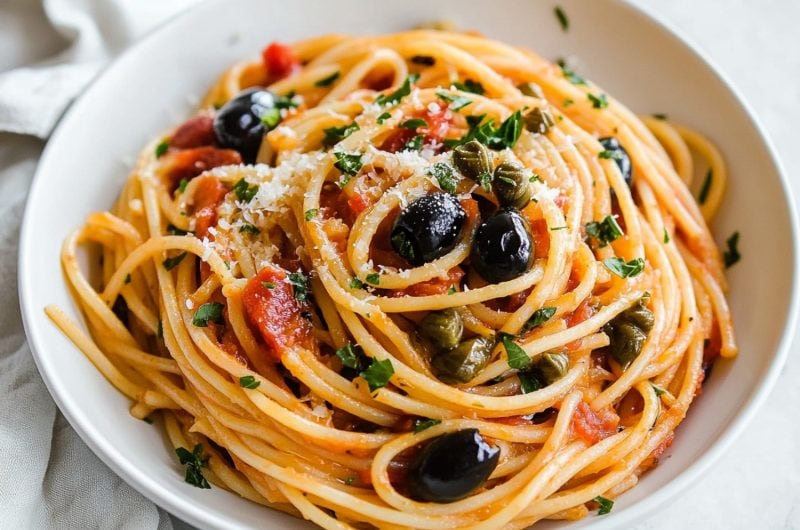 Pasta puttanesca serving garnished with grated parmesan cheese in a white bowl.