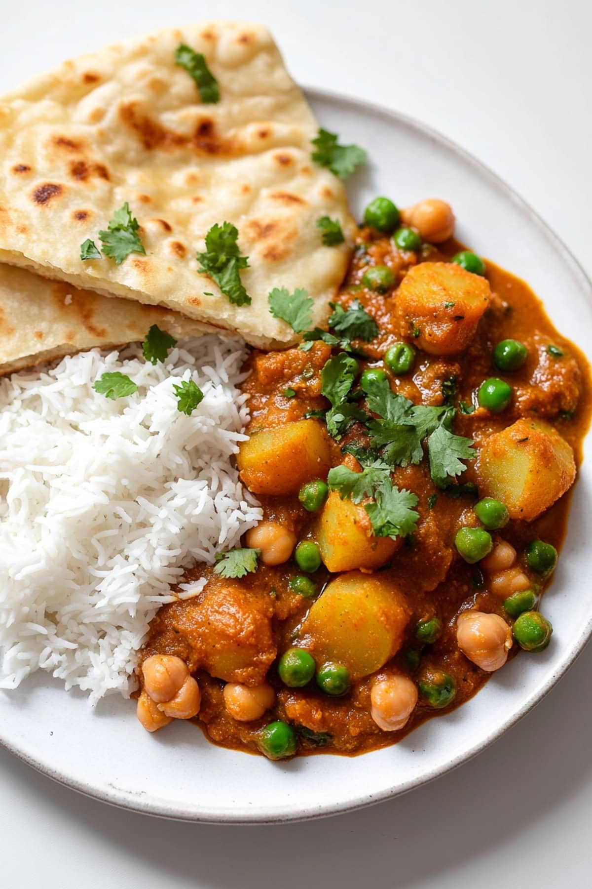 A warm plate of potato curry, garnished with fresh cilantro and served alongside steaming white rice and fluffy naan bread, top view